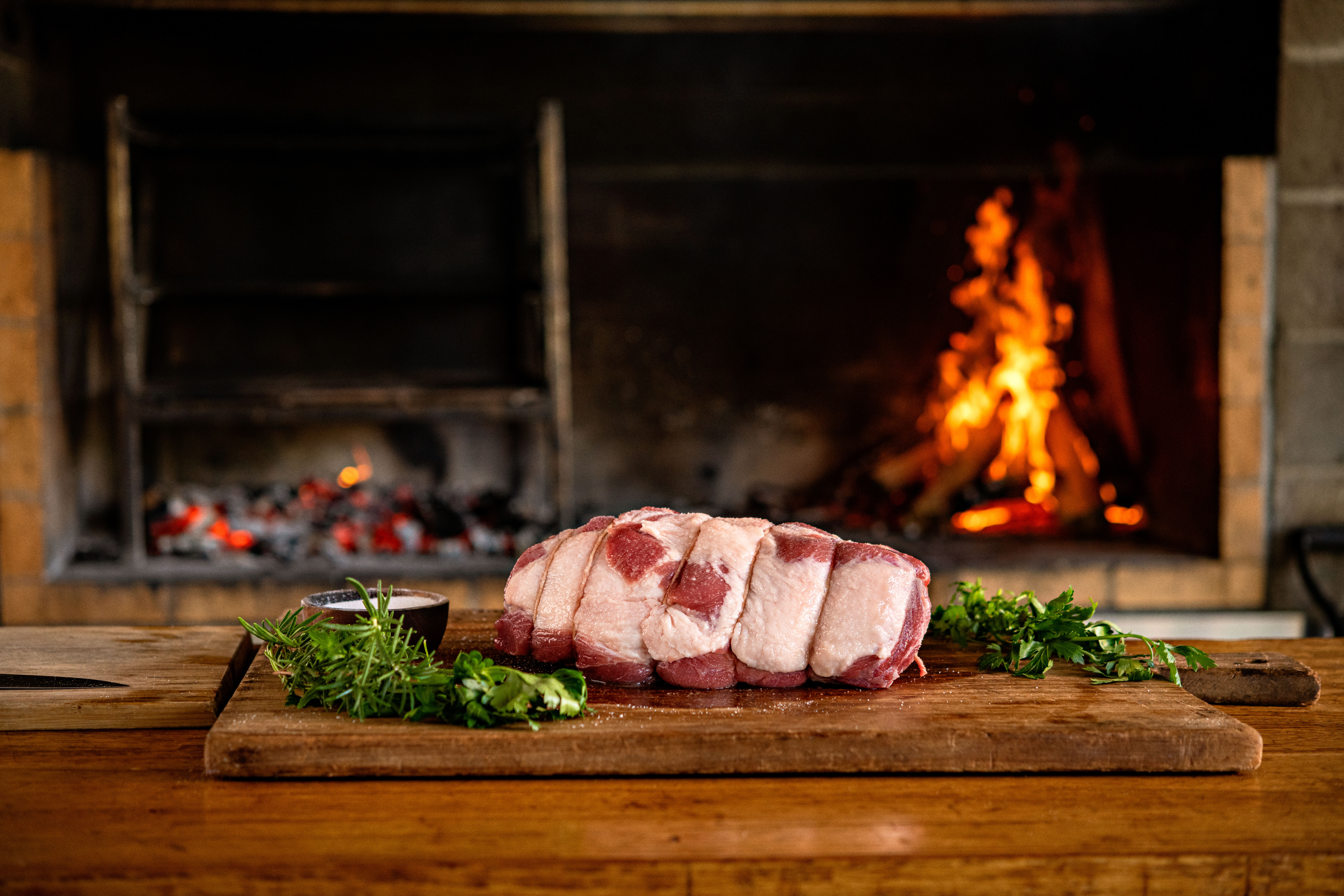 An elegant pork loin roast, wrapped in twine, ready to cook, sitting next to the fire.